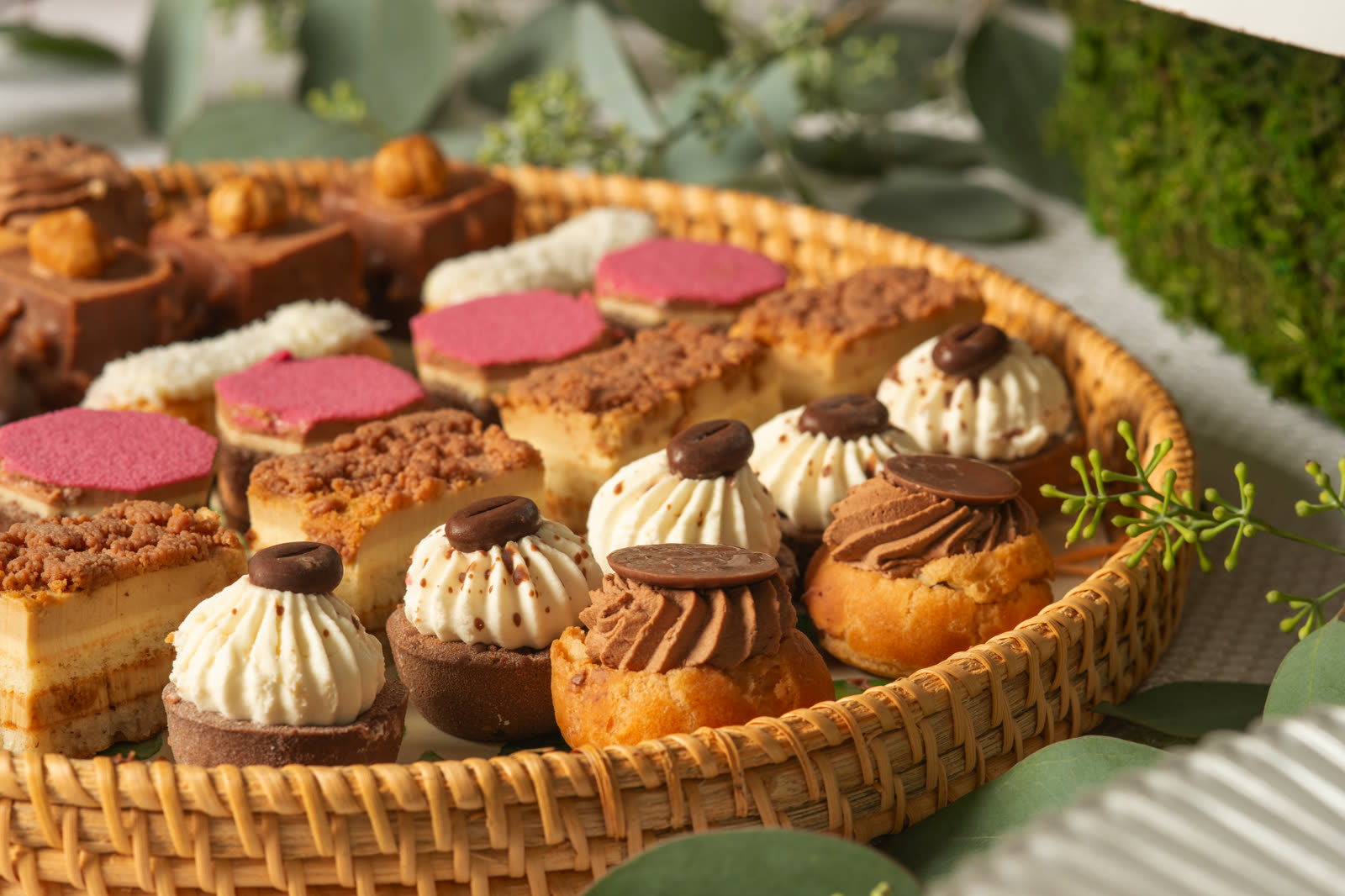 A woven tray of petite desserts — cream puffs, tortes, and pastries